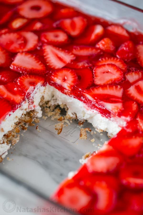 This strawberry pretzel salad is always a hit at parties. It's a strawberry jello dessert that is dangerously good! It's sweet, salty, tart and irresistible! #strawberrypretzelsalad #pretzelsalad #strawberrypretzeldessert #pretzeljellosalad #pretzelsaladrecipe #jello #strawberries #potluckdessert Pretzel salad sliced in a casserole dish showing layers of the pretzel salad