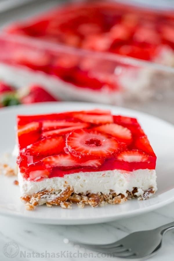 This strawberry pretzel salad is always a hit at parties. It's a strawberry jello dessert that is dangerously good! It's sweet, salty, tart and irresistible! #strawberrypretzelsalad #pretzelsalad #strawberrypretzeldessert #pretzeljellosalad #pretzelsaladrecipe #jello #strawberries #potluckdessert Slice of strawberry pretzel salad served on a plate with layers of pretzels, cream and strawberry strawberry jello dessert