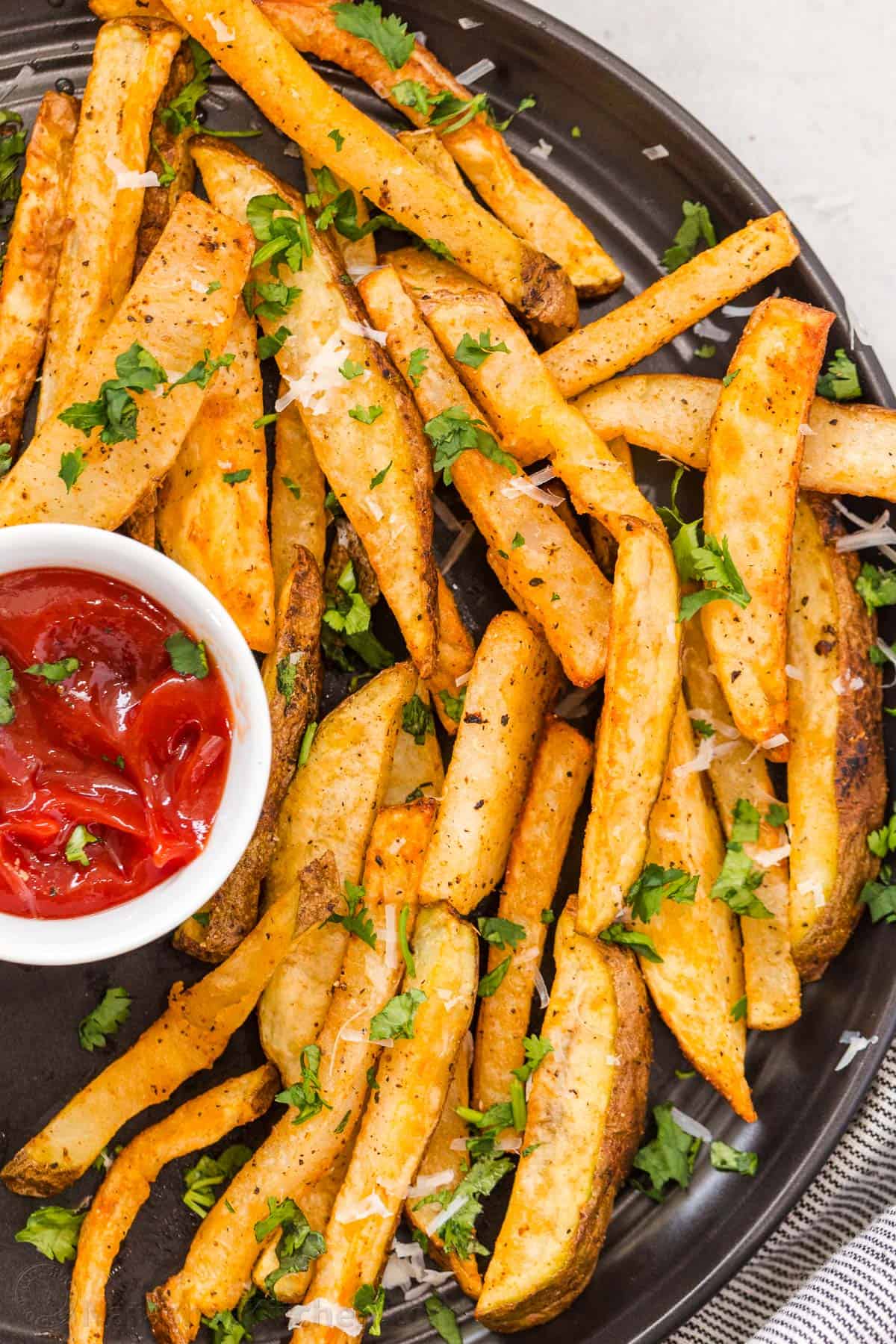 Homemade Air Fryer French Fries are so easy to make and taste much better than frozen fries! The Air Fryer makes it quick and easy to serve. Homemade Air Fryer French Fries on a black plate with parsley garnish and ketchup to dip