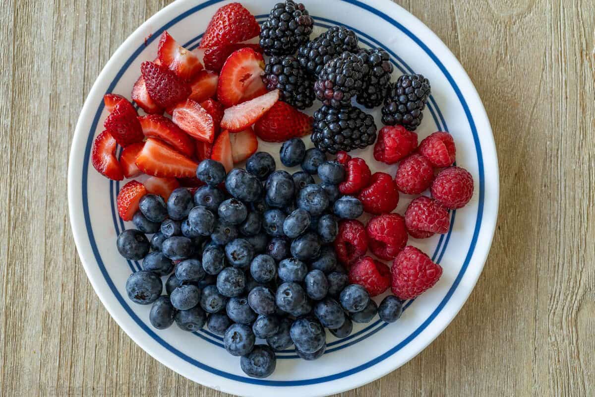 Easy Croissant French Toast Casserole with fresh berries is the best crowd-pleasing breakfast recipe. Refrigerate overnight for easy serving. cut strawberries, blackberrries, raspberries and blueberries on a white and blue plate