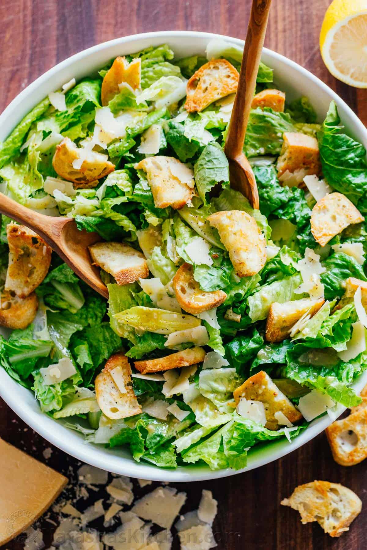 A classic Caesar Salad recipe with crisp romaine lettuce, fresh parmesan cheese, crunchy homemade croutons, and a light Caesar dressing. How to Make Caesar Salad tossing with 2 spoons in a bowl