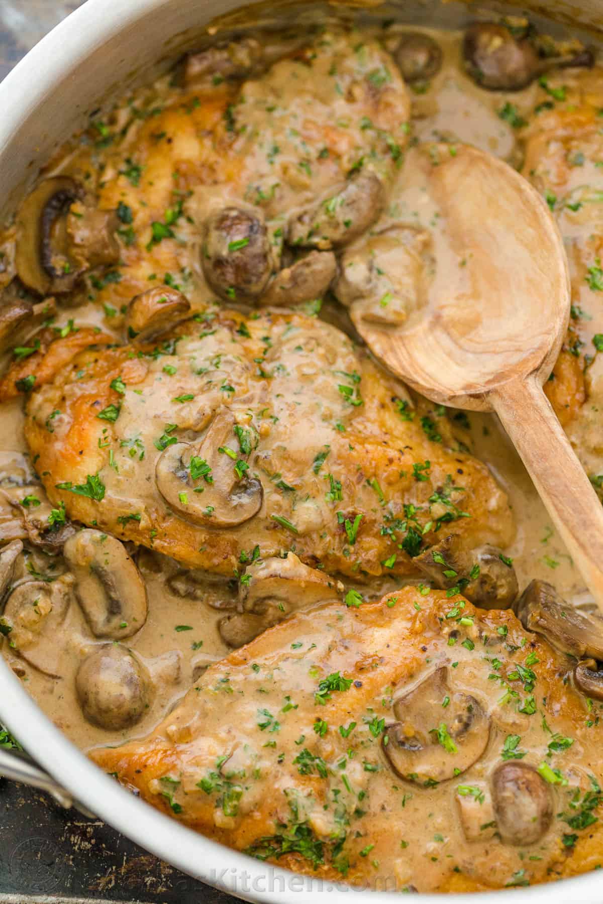This restaurant-quality Chicken Marsala is an easy 30-minute recipe (with Video Tutorial). Juicy pan-fried chicken topped with a creamy marsala wine sauce. #chickenmarsala #chickenmarsalarecipe #natashaskitchen Chicken Marsala in a pan with a wooden spoon topped with mushrooms and parsley.