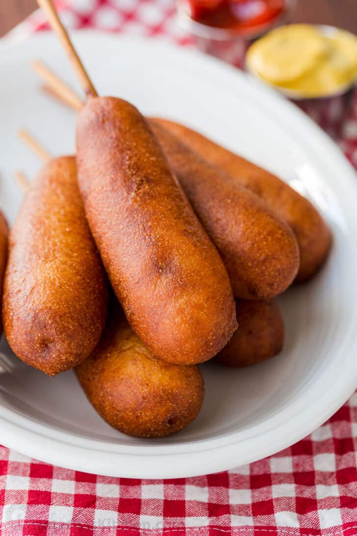 Honey-battered, hand-dipped Corn Dogs are a real treat. Watch the video tutorial and see how easy it is to make homemade corn dogs from scratch. homemade corn dogs on a serving plate with ketchup and mustard
