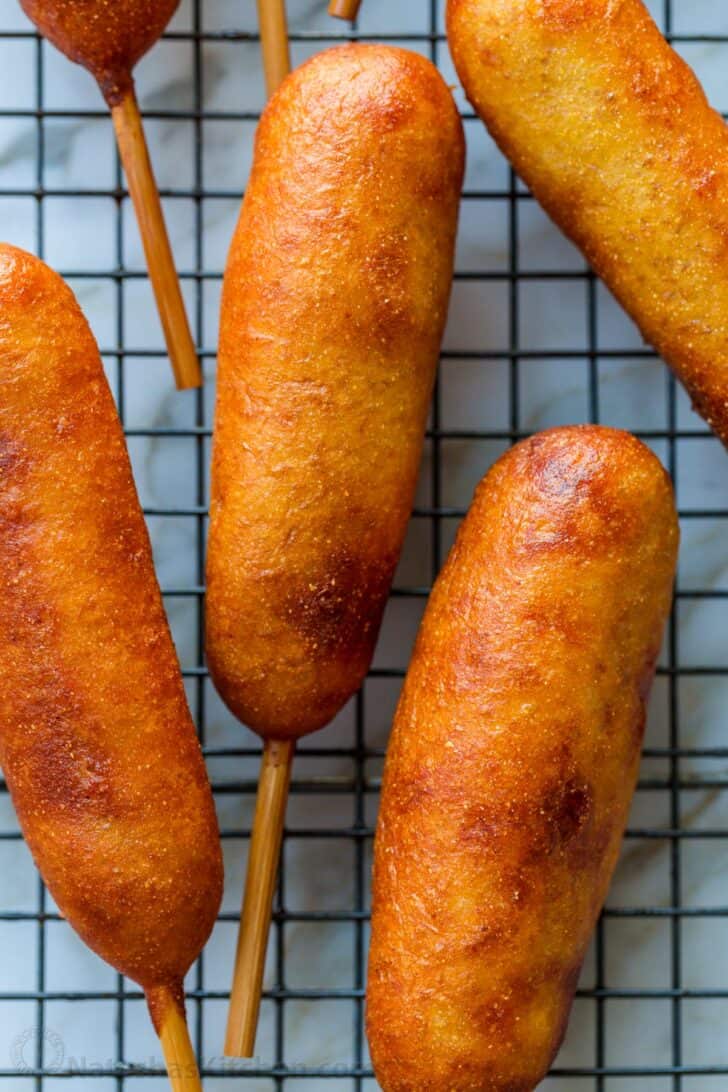 Honey-battered, hand-dipped Corn Dogs are a real treat. Watch the video tutorial and see how easy it is to make homemade corn dogs from scratch. corn dogs cooling on a wire rack