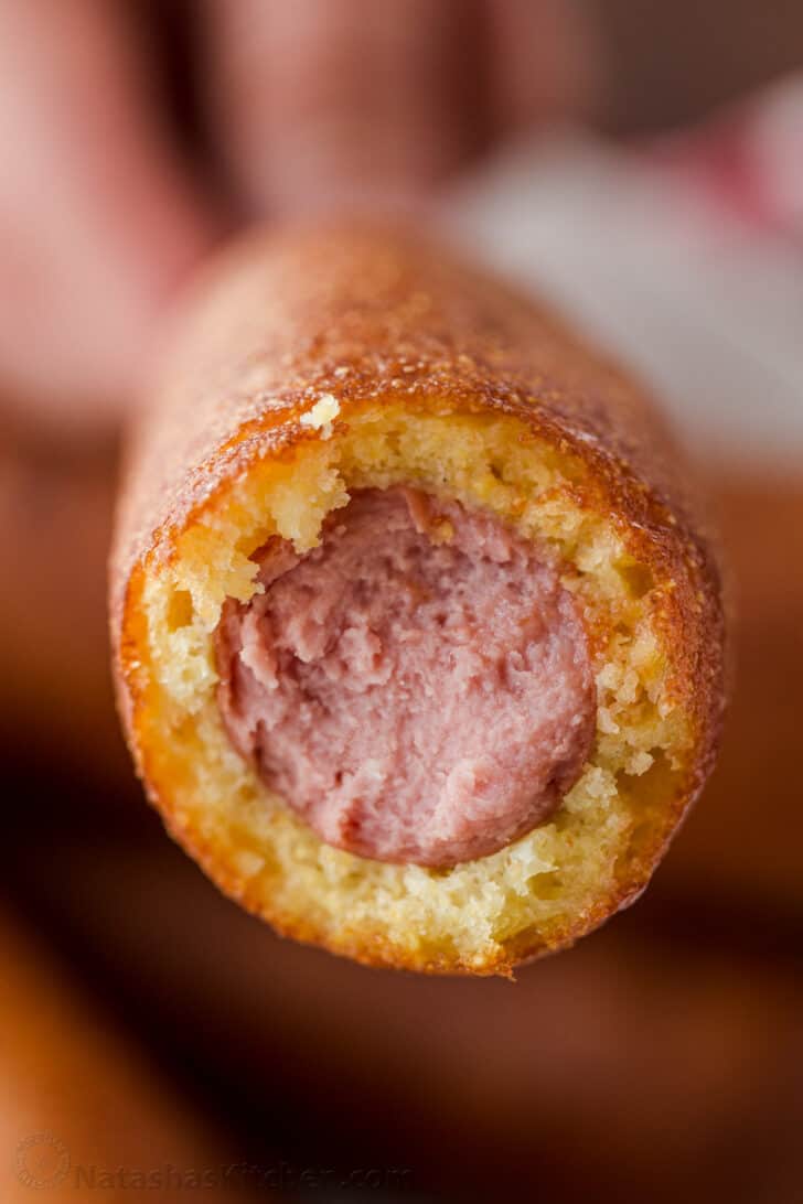 Honey-battered, hand-dipped Corn Dogs are a real treat. Watch the video tutorial and see how easy it is to make homemade corn dogs from scratch. bitten corn dog showing sausage and corn bread center