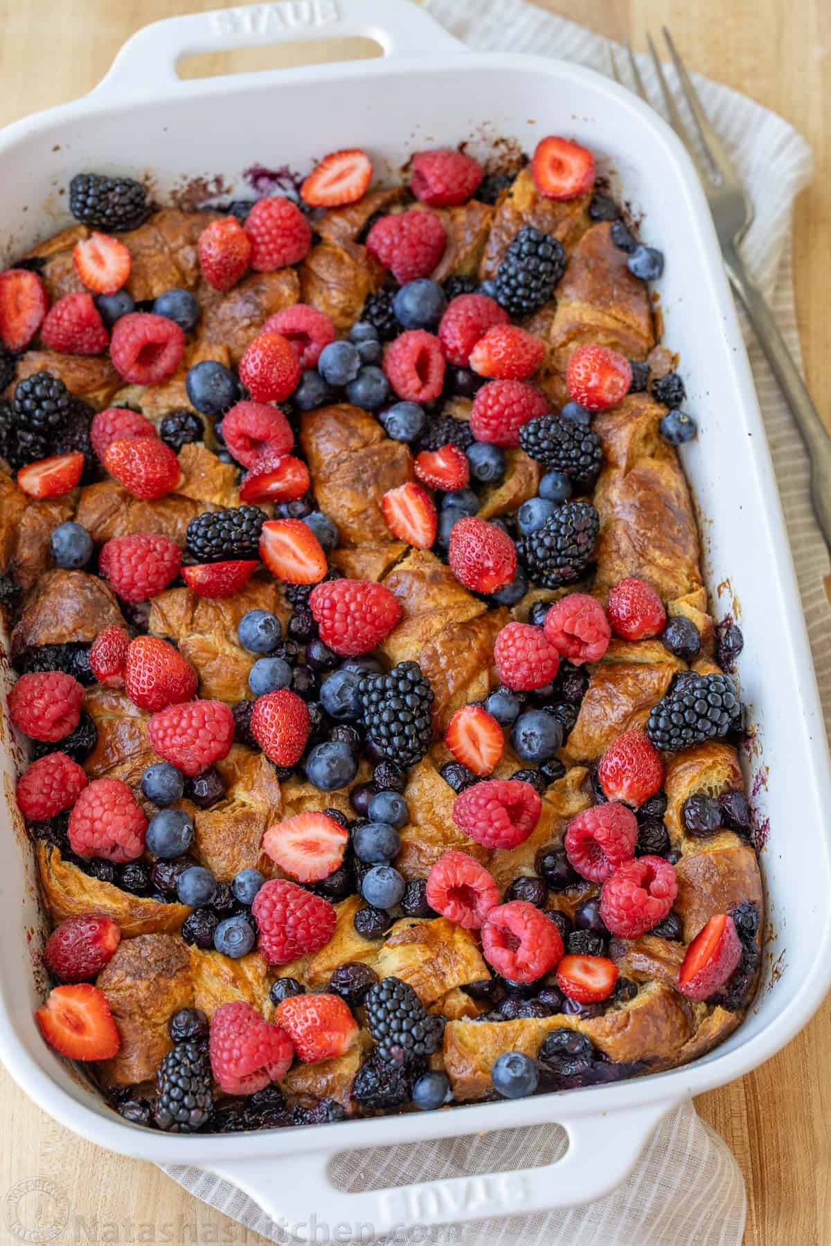Easy Croissant French Toast Casserole with fresh berries is the best crowd-pleasing breakfast recipe. Refrigerate overnight for easy serving. Berries and cut strawberries scattered over Croissant French Toast Bake in a white dish