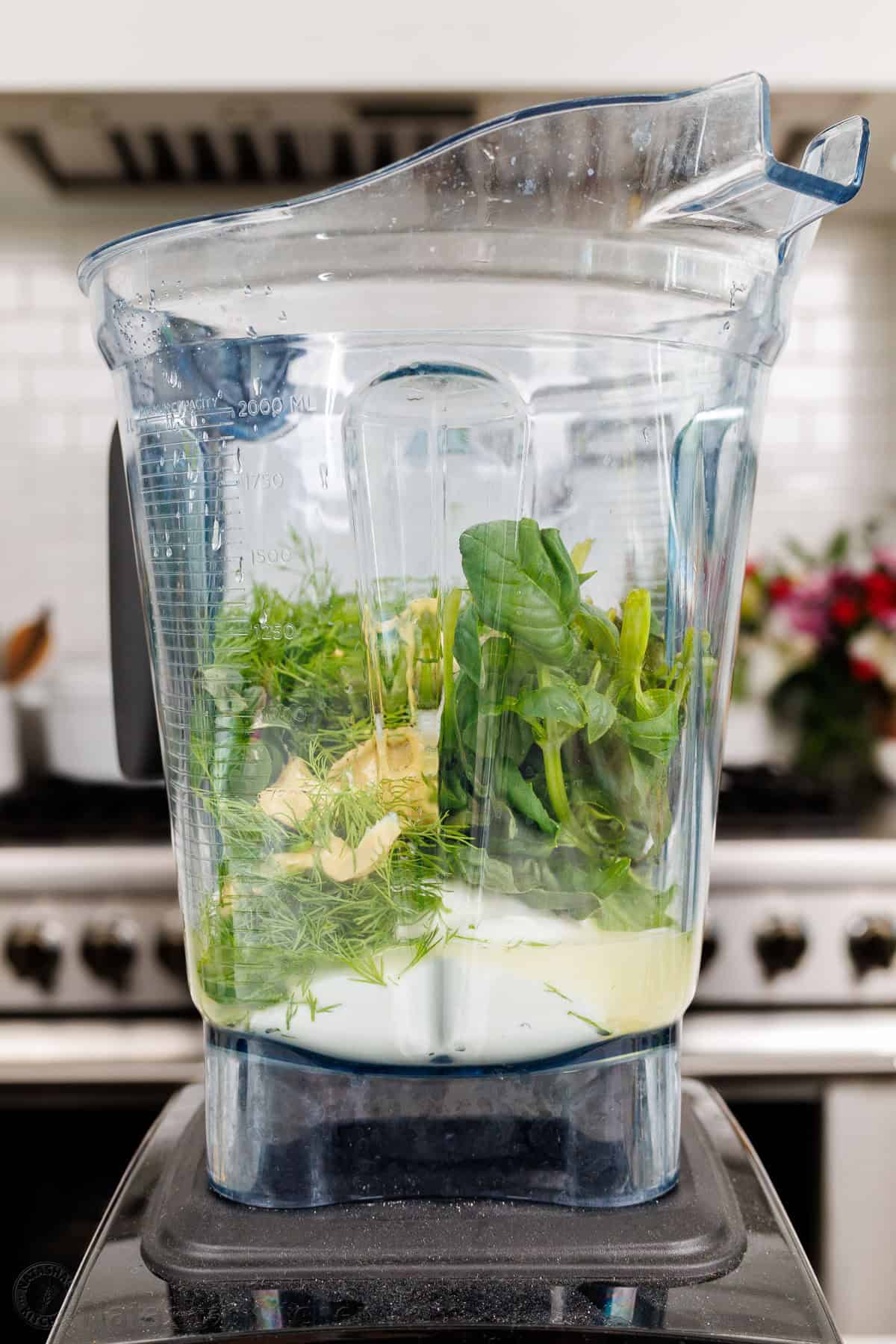 Homemade Green Goddess Dressing is easy to make and tastes so fresh and vibrant. It takes just 30 seconds from blender to topping salads! Ingredients for Green Goddess Dressing in a blender including fresh herbs, Greek Yogurt, seasoning, and mustard