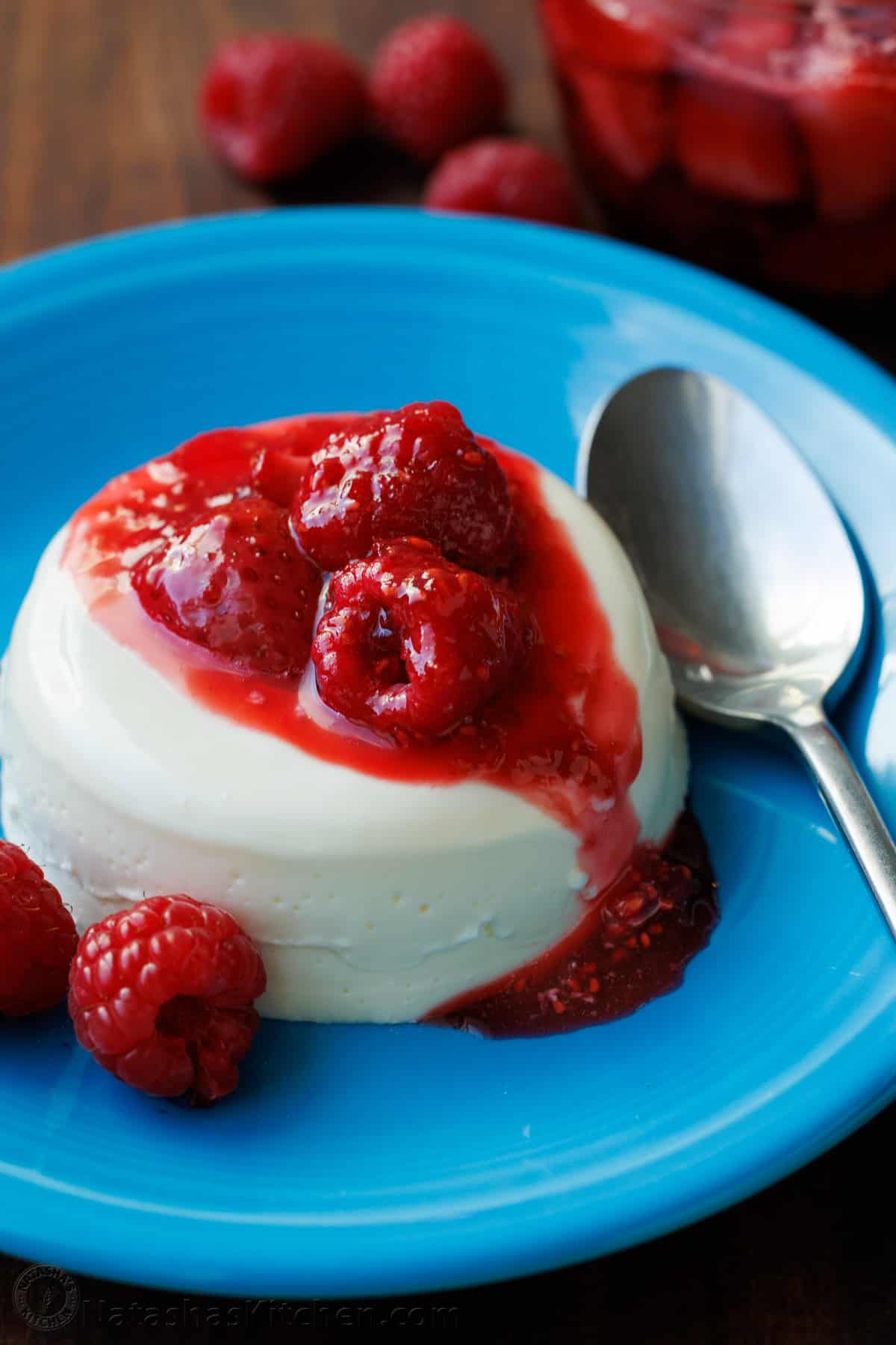 Panna Cotta is an Italian dessert that looks and tastes fancy but is so quick and easy to make! The fresh berry sauce gives every creamy spoonful the perfect balance of sweet and tangy. Panna Cotta with berry sauce drizzled on top, sitting on a blue plate with a spoon.