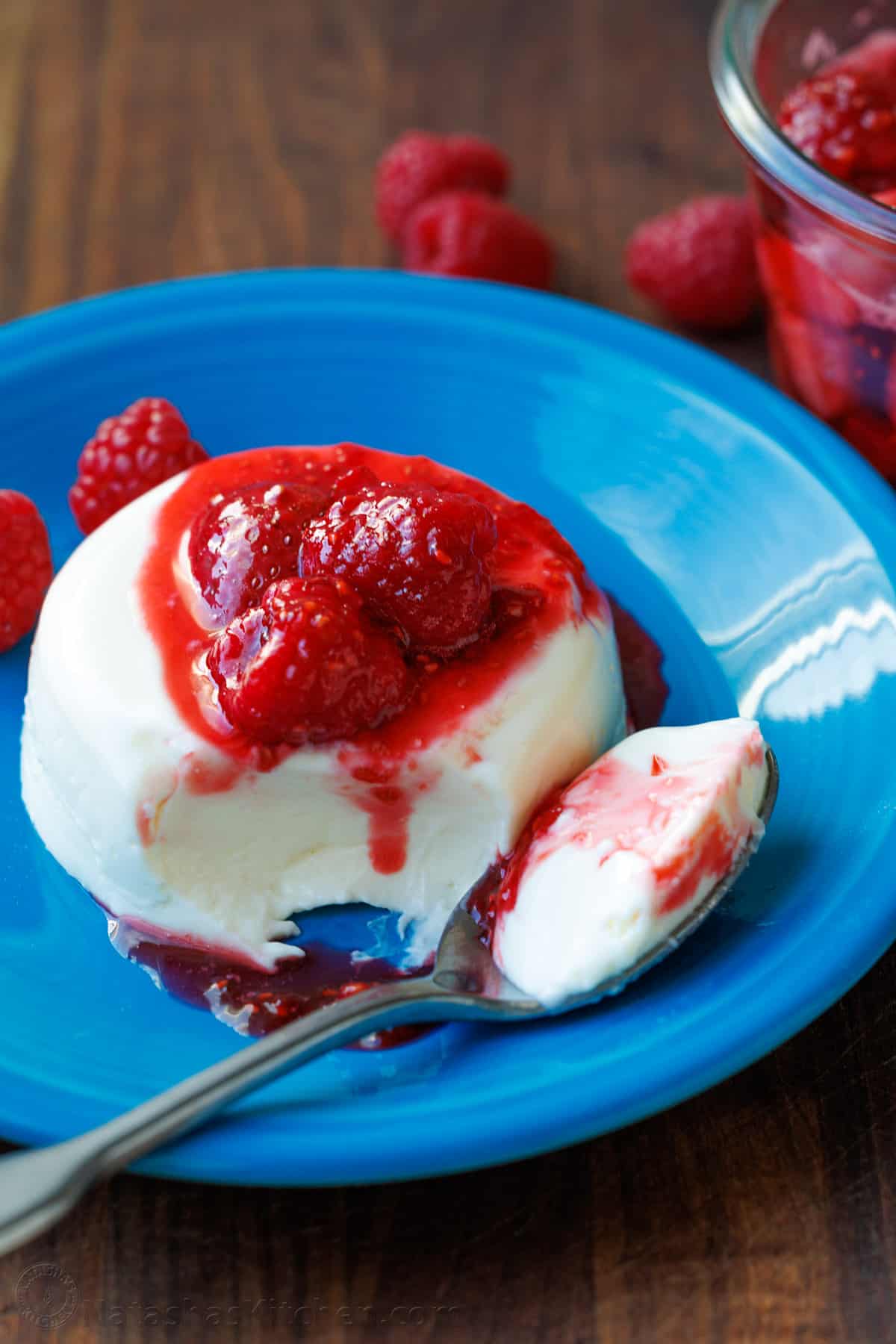 Panna Cotta is a quick and easy Italian dessert. The fresh berry sauce gives every creamy spoonful the perfect balance of sweet and tangy. Panna Cotta with fresh berry sauce cascading down the side with one bite loaded onto a spoon laying on a blue dessert plate.