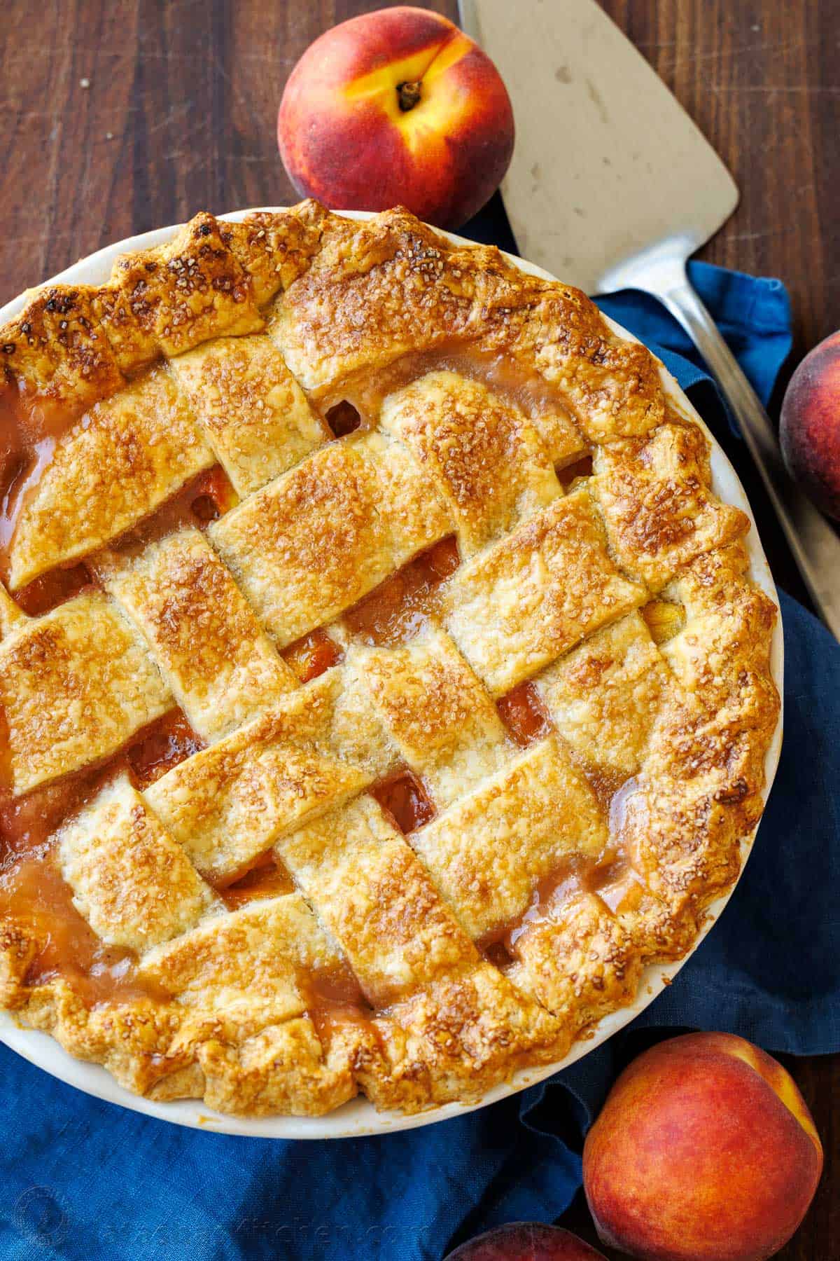 Easy homemade Peach Pie Recipe with pie crust made from scratch. This fool-proof recipe tastes amazing with ripe peaches. Gets rave reviews! Peach Pie recipe with lattice crust on a blue table cloth with a pie server.