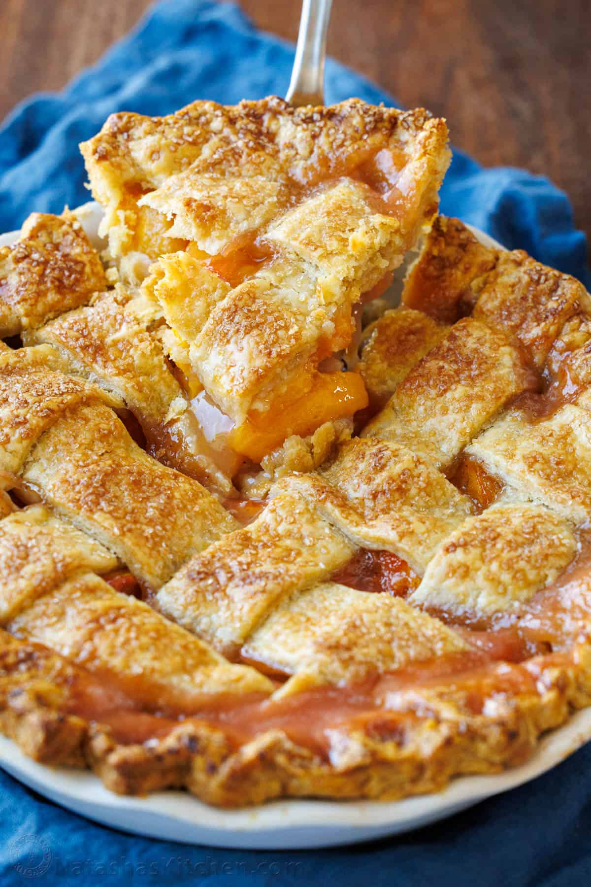 Easy Peach Pie Recipe with a flaky homemade pie crust. This fail-proof recipe is loaded with ripe juicy peaches and always gets rave reviews! Slice of peach pie lifting out of the dish with blue napkin