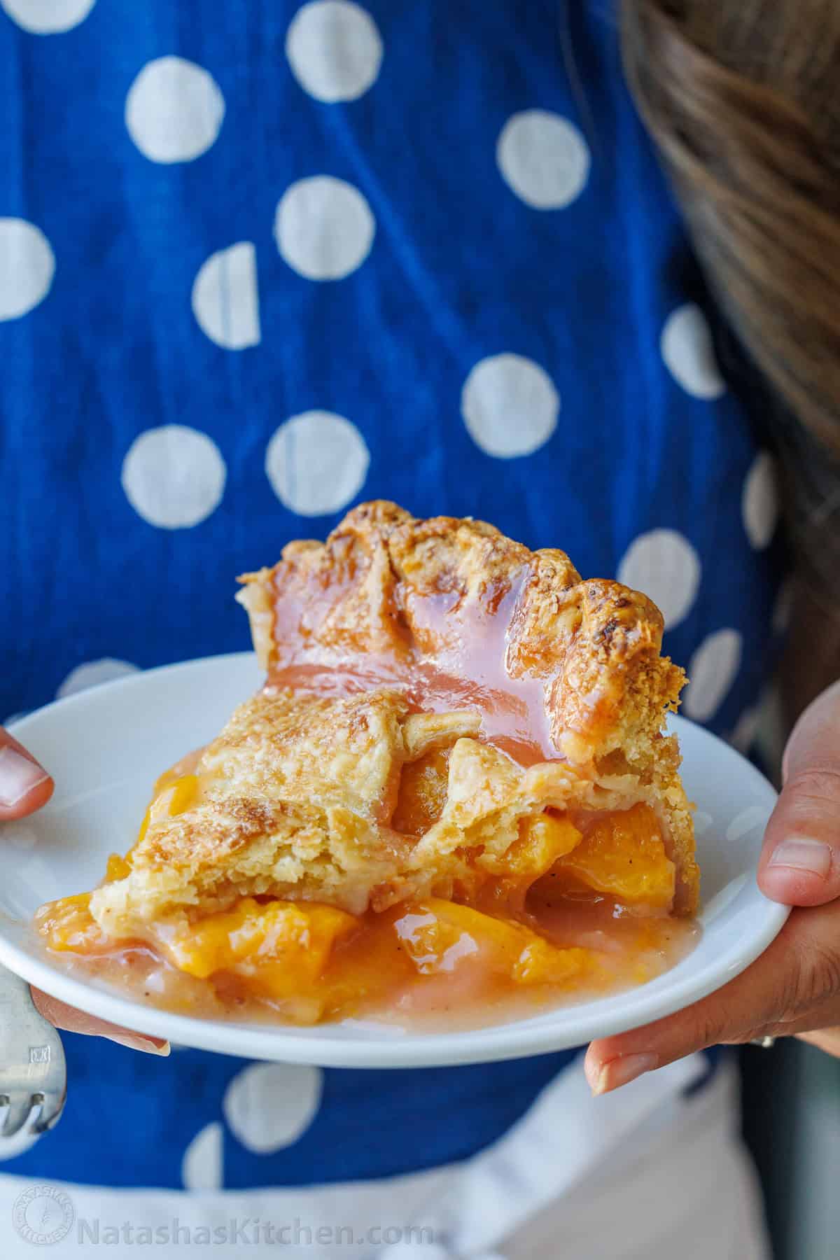 Easy homemade Peach Pie Recipe with pie crust made from scratch. This fool-proof recipe tastes amazing with ripe peaches. Gets rave reviews! Plate of fruit dessert carried by a woman