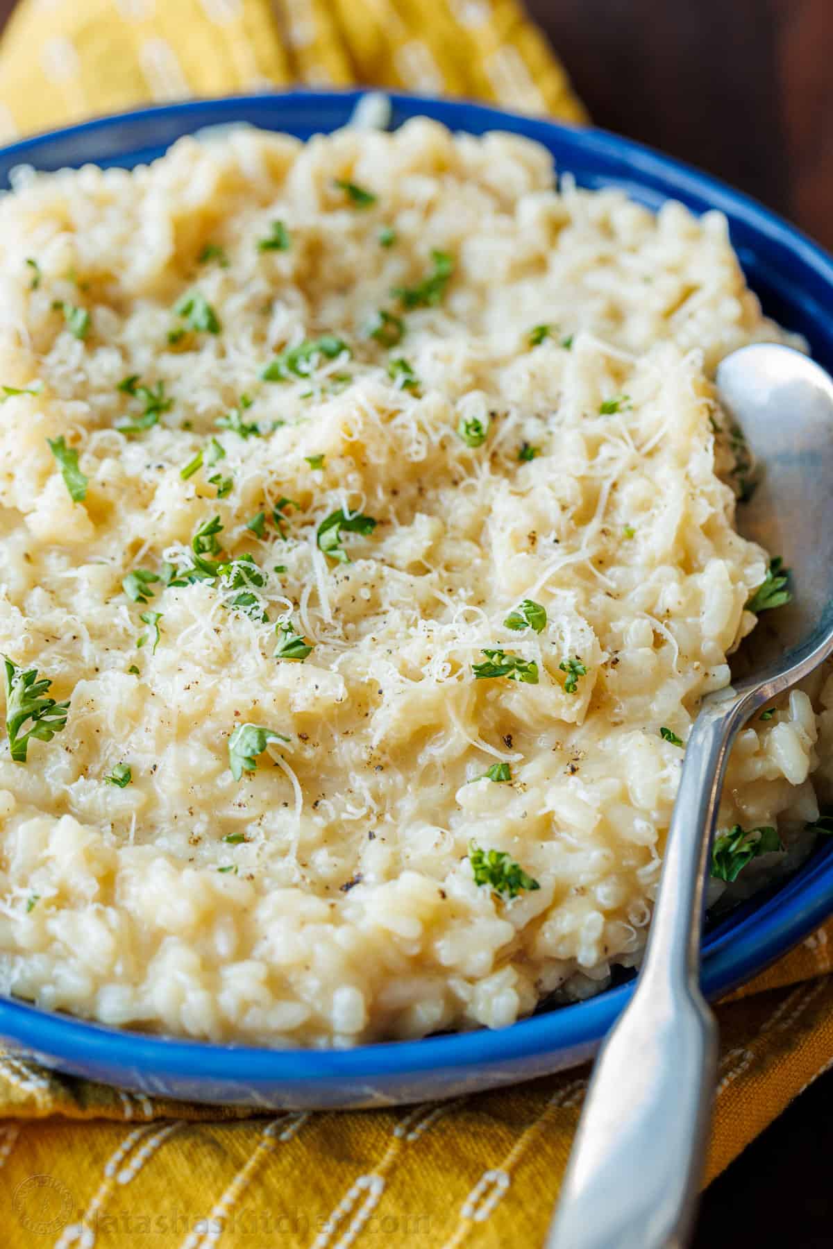 Creamy parmesan Risotto is the ultimate side dish. Learn how to make the best Risotto that can be modified in many different ways. Risotto in blue bowl garnished with parmesan and parsley