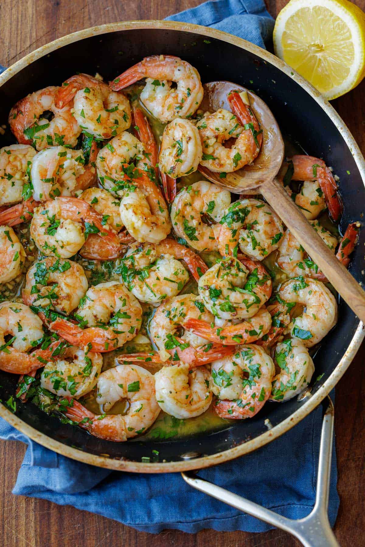 Shrimp Scampi Recipe with garlic, butter, and wine sauce drizzled with fresh lemon juice. This easy shrimp scampi takes just 10 minutes! shrimp scampi recipe cooked in a sauté pan on the stove with a wooden spoon and garnished with parsley