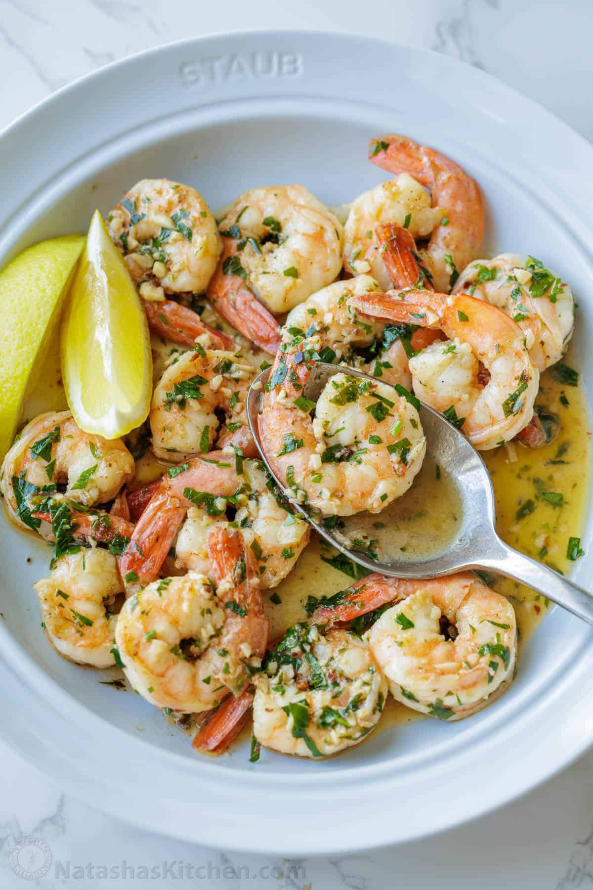 Shrimp Scampi Recipe with garlic, butter, and wine sauce drizzled with fresh lemon juice. This easy shrimp scampi takes just 10 minutes! Spoon serving shrimp scampi from a white dish with garlic butter sauce and lemon wedges