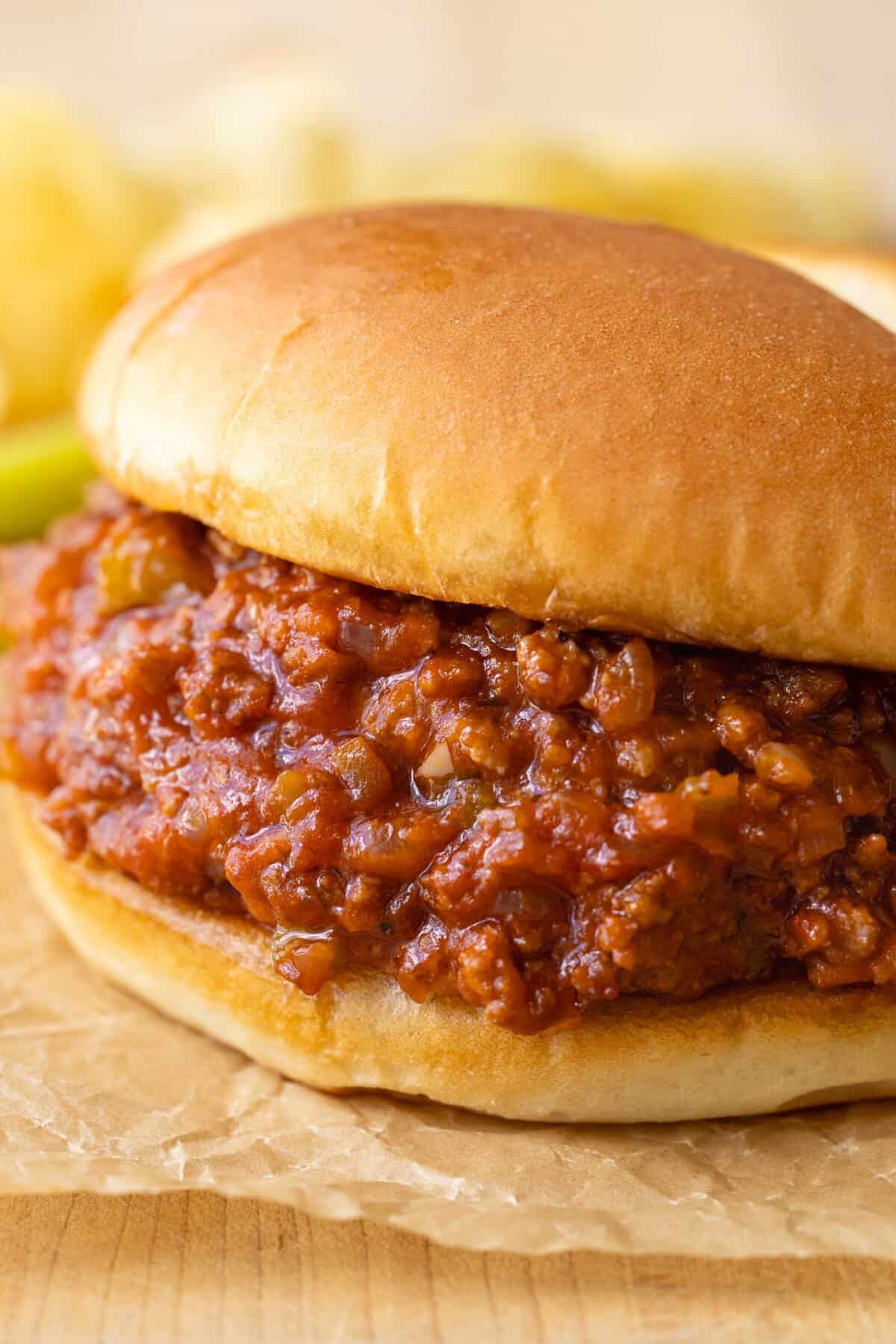 The BEST homemade sloppy joes recipe that is easy to make and loaded with flavors from the rich and flavorful tomato sauce. Sloppy Joe up close with saucy sloppy joe filling on a bun served with pickles and chips