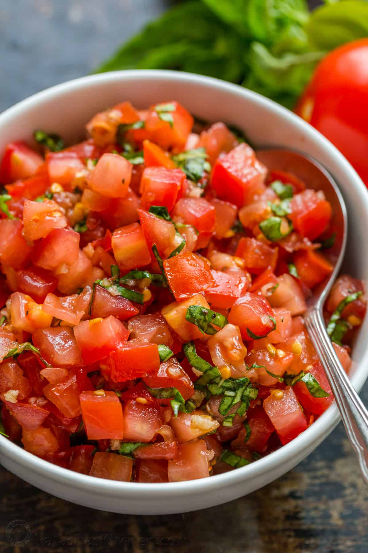 Authentic Italian Bruschetta! Learn how to make a crowd-pleasing tomato bruschetta. The parmesan toasts and drizzle of balsamic make these irresistible. Tomato bruschetta topping in a bowl