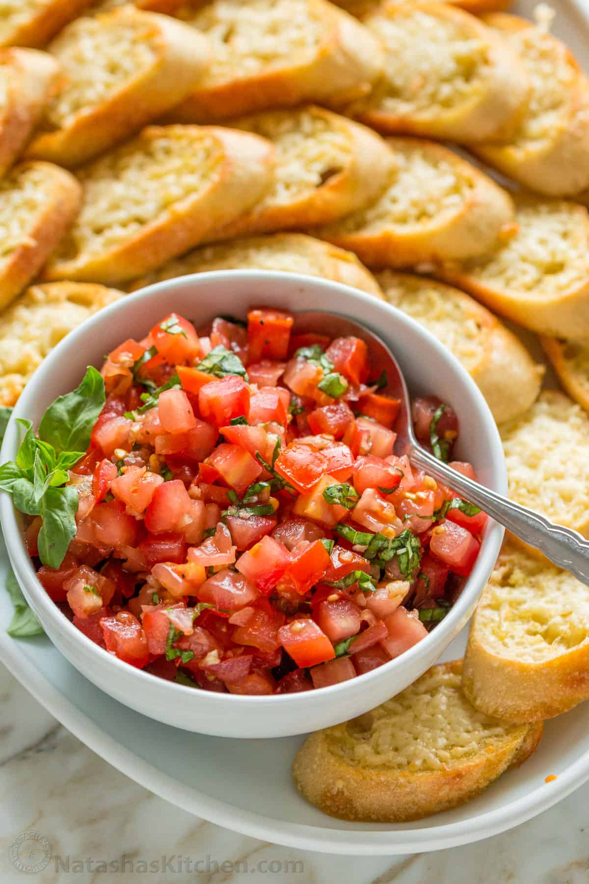 Authentic Italian Bruschetta! Learn how to make a crowd-pleasing tomato bruschetta. The parmesan toasts and drizzle of balsamic make these irresistible. Bruschetta toasts served on a platter with a bowl of tomato topping