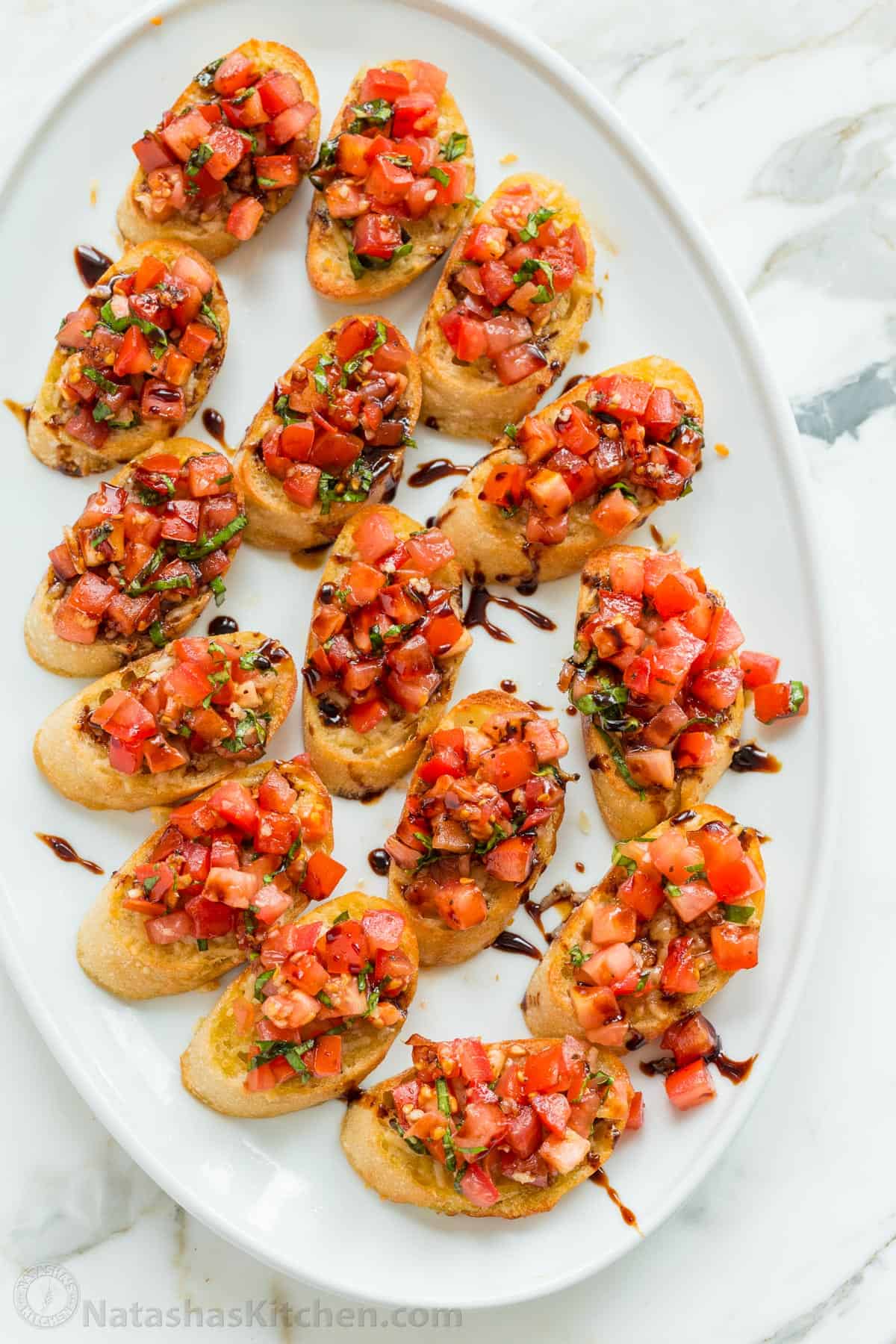 Authentic Italian Bruschetta! Learn how to make a crowd-pleasing tomato bruschetta. The parmesan toasts and drizzle of balsamic make these irresistible. Italian Tomato Bruschetta served on a platter
